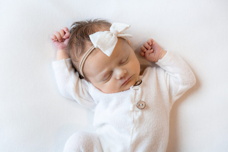 Newborn, baby girl with white bow and white outfit on a beanbag during her professional newborn photography session in Huntsville, Alabama.